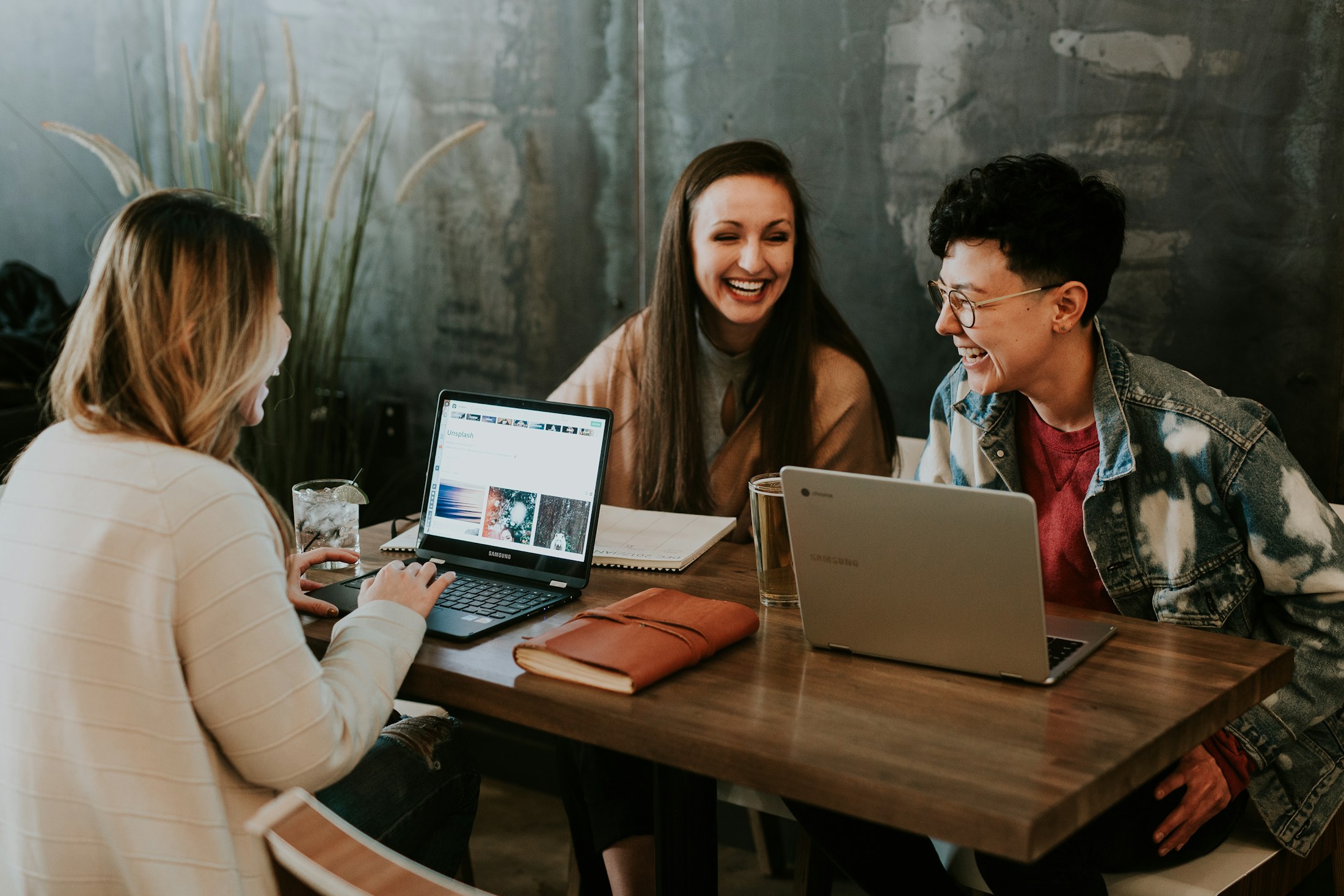 Three cohort members laughing together during a workshop over laptops